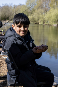 A boy from Nature Warriors holds a fish by a lake