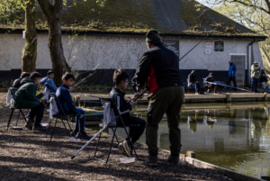 Nature Warriors group of young people from Greater Manchester enjoy a coaching session at Boggart Hole Clough. The picture shows a lake, 4 boys and Coach Duncan